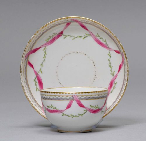 TEA CUP AND SAUCER WITH PURPLE BAND,Nyon, ca. 1781-1813. Painted with a purple fabric garland with green leaf garland and braided and in grisaille between gold borders. Underglaze blue fish marks. Gilding, slightly rubbed. Provenance: Private collection, Geneva.