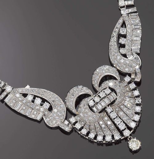 DIAMOND NECKLACE, ca. 1950. Platinum and white gold 750. Very fancy "Rivière" necklace in the Art Deco style, the top decorated with stylized band and volute motives around a fan-like middle part, entirely set with ca. 275 brilliant-cut diamonds and octagonal-cut diamonds totalling ca. 20.00 ct and 24 baguette-cut diamonds totalling ca. 1.80 ct. The end consists of 1 movably mounted brilliant-cut diamond of ca. 1.20 ct. L ca. 43 cm.