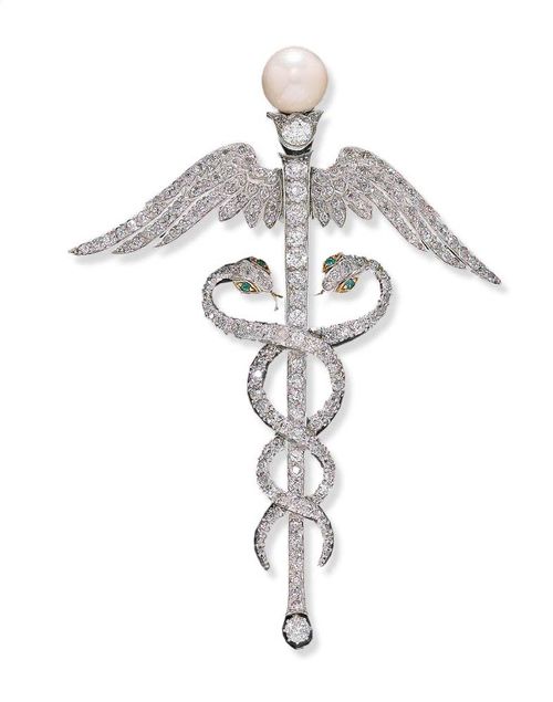 DIAMOND AND PEARL BROOCH, ca. 1910. Platinum over yellow gold. Very decorative, large brooch, in the shape of Mercury's staff, the staff with its two entwined snakes and the wings completely set with 184 old-mine cut diamonds totalling ca. 3.50 ct, a pearl of ca. 10 mm Ø on its top, 4 small emeralds for the eyes of the snakes. Removable brooch part. L ca. 9 cm.