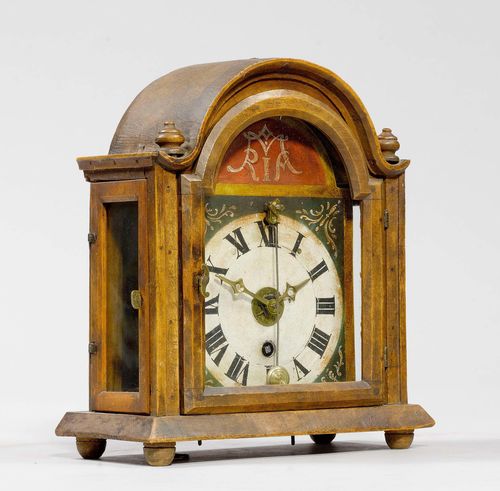 SMALL TABLE CLOCK WITH FRONT PENDULUM AND ALARM,in the Baroque style, 19th century. Wooden case, glazed on three sides. Baroque design, on spherical feet. Painted metal dial. Brass cog wheels, movement with verge escapement, and alarm on bell. 23x11.5x26 cm.