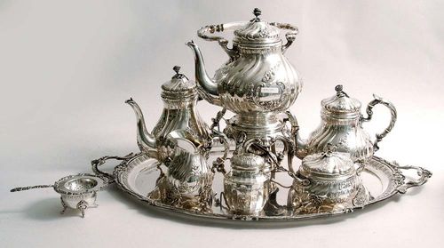 COFFEE AND TEA SERVICE. Germany after 1900.Decorated with vertical folds and cartouches with rocaille and scrolls. The domed lids with rose finial. Comprising: coffee pot, teapot, kettle and heater, cream jug, sugar bowl, tea caddy and large oval tray. H coffee pot 24 cm. Total 7650 g.