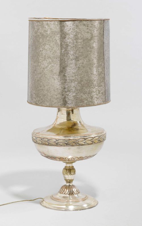 LARGE TABLE LAMP,Italy, in the Baroque style. Copper, painted silver. Amphora-shaped base with circumferential leaf frieze. Silver fabric shade. On a round plinth. H 55 cm. Fitted for electricity.