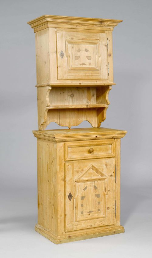 BUFFET,in the Baroque style, from the Alpine region. Pinewood, inlaid with architectural bow motifs. 2 parts. The upper part is a wall-cupboard with a rectangular body and a protruding rim, with one door over a shelf. 74x35x91 cm. The lower part has a rectangular body with one drawer and one door. Iron mounts. 65x43x88 cm. 2 keys.