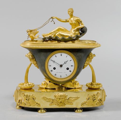 MANTEL CLOCK,Empire, Paris, ca. 1810. The dial signed AL. MONTHELIER À PARIS. Gilt bronze, in part burnished. Bowl-shaped case on a base designed as 2 dolphins, oval plinth with spherical feet. White enamel dial (chipped). Parisian movement striking the 1/2-hour on bell. H 35 cm. Gilding later.