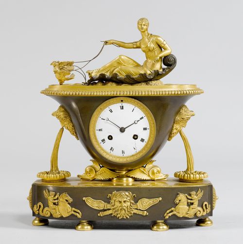MANTEL CLOCK,2nd Empire, France, 19th century. Gilt bronze, in part burnished. Bowl-shaped case on a base designed as 2 dolphins, with an oval plinth on spherical feet. On top: a woman in a shell-shaped boat, pulled by 2 birds. White enamel dial (cracked). Parisian movement, striking the 1/2-hour on bell. H 35 cm. Pendulum defective.
