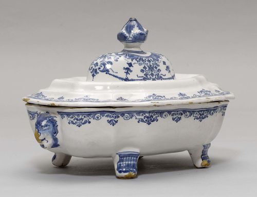 FAIENCE LEGUMIER,Moustier, 18th century. Oval vegetable pot on lion paw feet and with lion heads on the side. Painted blue with a lambrequin border. Cover with artichoke finial. L 30 cm. Losses in the glaze.