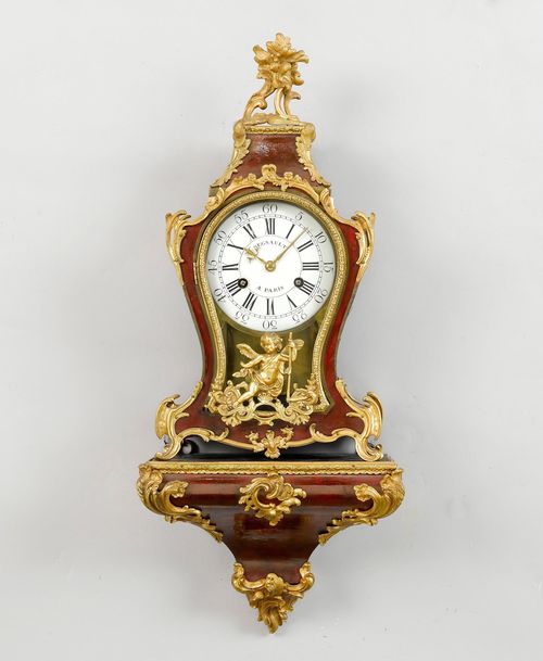 SMALL CLOCK ON PLINTH, Regence/Louis XV, Paris, 2nd half of the 18th century. The dial and movement signed REGNAULT À PARIS (Pierre Renault, witnessed in Paris 1768-89). Curved, wooden case with red tinted horn. Bronze mounts designed as leaves, rocailles, flowers and angels. White enamel dial with the hours in Roman numerals and the minutes in Arabic numerals. Movement with verge escapement, striking the 1/2-hour on bell. H 81 cm. Restored.