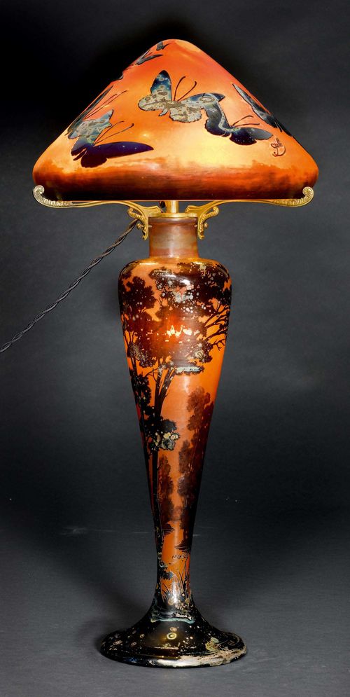 EMILE GALLE TABLE LAMP, ca. 1900. Orange glass with violet overlay and etching. Mushroom-shaped lamp, decorated with trees and butterflies. Signed Gallé. H 65 cm.