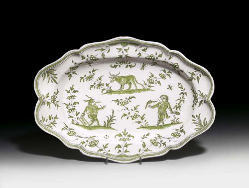 OVAL DISH 'AU CALLOT', Moustier, Olérys, mid 18th century. Painted in green camaïeu and edged in manganese, with grotesques and bull between flowering branches and tendrils. Cross mark in blue. D 43cm. Provenance: private collection, South Germany