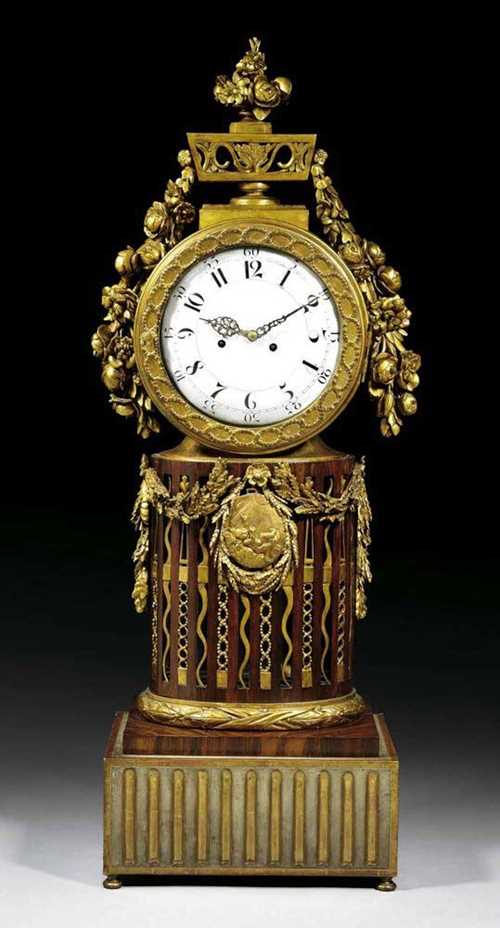 IMPORTANT CLOCK WITH CARILLON, Louis XVI, the movement signed I.E. BAUMGARTINGER MERGENTHEIM (Johann Erasmus Baumgartinger, 1748-1811), Germany circa 1785/90. Richly carved wood with flowers, leaves, garlands, laurel and frieze, and partly painted in gold and grey. The drum-shaped case with pierced floral cresting and floral sprays on pierced oval column with central medallion. The clock with enamel dial, 2 pierced hands, fine verge escapement with 4/4 striking on 2 bells, with carillon with 8 melodies and 11 bells released on the hour. H 130 cm. Provenance: from a Dutch collection.