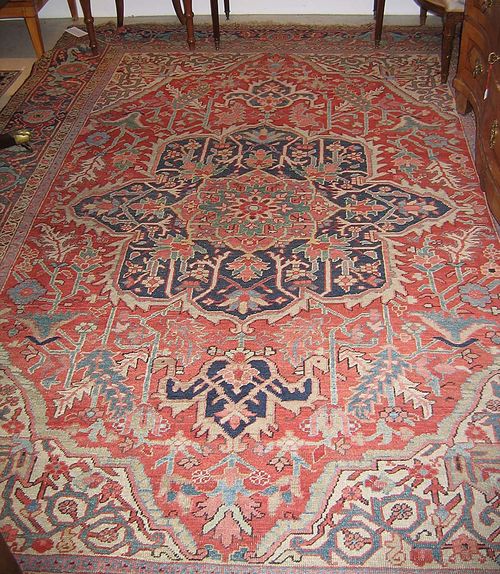 HERIZ antique. Large central medallion in blue on red ground with white corner motifs, the whole carpet decorated with stylised plant motifs, dark border, considerable wear. 290x210 cm.