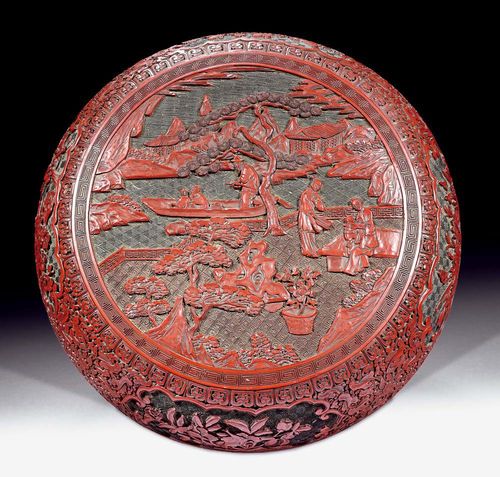 LARGE ROUND BOX WITH LID.China, 18th/19th century. D 30.8 cm. Made of two-tone carved lacquer, red on black. Depiction of court ladies in a garden landscape, with three people in a boat in the background. On the wall, eight spaces with floral decorations on a background of dense lotus tendrils. Slightly rubbed on the inside. Short fissures on the lower edge of the container.