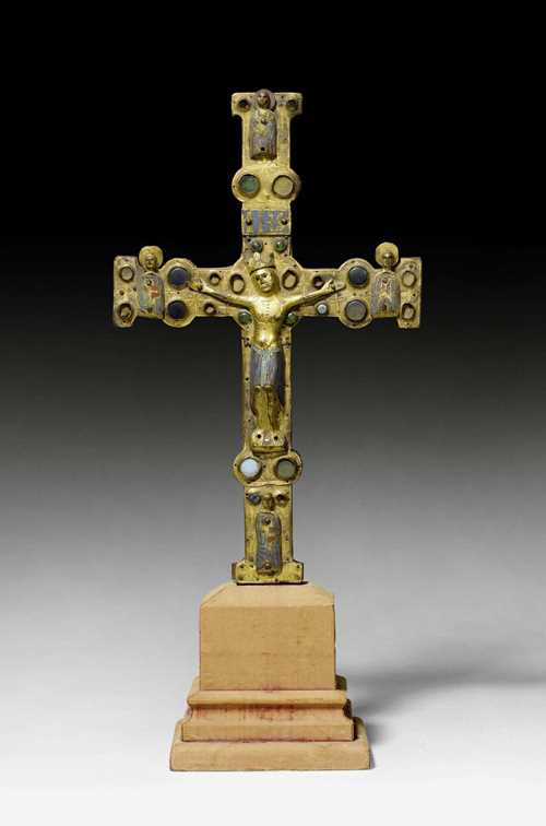 PROCESSIONAL CROSS,Limoges, early 13th century. Wooden core mounted with chased and gilt copper, set with glass stones and champleve enamel plaques in turquoise, dark blue, red and green. The Corpus Christi in engraved, gilt and enameled copper. One side of the cross with the crucified Christ and half-figures of the Evangelists at the cross ends. Verso with round, enamel plaque of Christ in Majesty. The cross ends with the symbols of the Evangelists. Losses and chips. Supplements. H 41 cm.