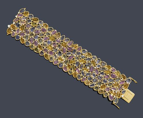 MULTICOLOR SAPPHIRE AND DIAMOND BRACELET. Yellow and white gold 750, 98g. Fancy, open-worked bracelet, set with numerous sapphires of different shapes and sizes in yellow gold collet settings. Total sapphire weight ca. 99.00 ct. The intermediate spaces are additionally decorated with 73 brilliant-cut diamonds set in white gold chatons. Total weight of the diamonds ca. 1.00 ct. W ca. 4 cm, L ca. 17.5 cm. With case.