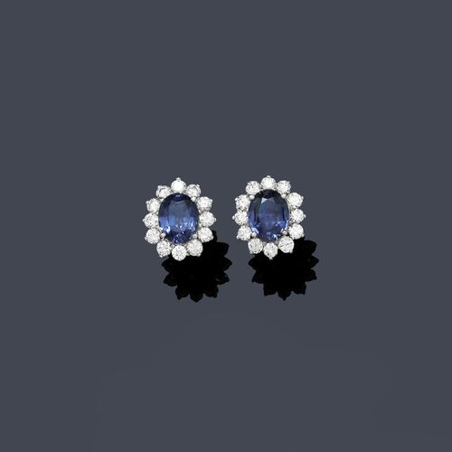SAPPHIRE AND DIAMOND EAR STUDS. White gold 750. Classic elegant ear studs, each set with 1 oval sapphire. Total weight of the sapphires 7.51 ct, set within a border of brilliant-cut diamonds of ca. 2.20 ct. Matches the following lot.