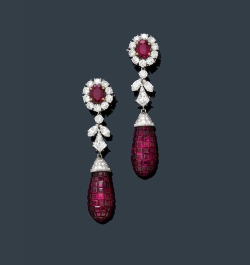 RUBY AND DIAMOND EAR PENDANTS. White gold 750 and platinum. Elegant ear clips, each set with 1 oval ruby, weighing ca. 3.50 ct in total, each within a border of 10 brilliant-cut diamonds, weighing ca. 3.00 ct in total. The lower ornamental part, each with 1 diamond in a fantasy cut, 1 brilliant-cut diamond and 2 navette-cut diamonds, weighing ca. 2.20 ct in total, as well as 2 drop-shaped pendants, set throughout with numerous square-cut rubies, weighing ca. 12.00 ct in total, invisible setting, and 24 small diamonds. L ca. 6.5 cm. With case.