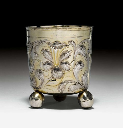 FOOTED BEAKER,Nuremberg ca. 1680. Maker's mark probably Johann Höfler. On three spherical feet. Wall with chased floral decoration, parcel- gilt. Profiled lip edge. Some repairs. H. 8.5 cm, 75g. Provenance: German private collection.