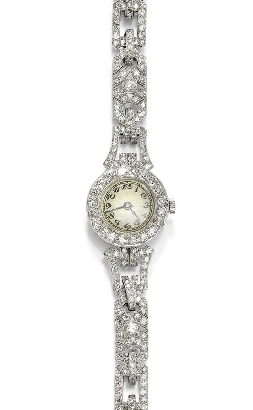 DIAMOND LADY'S WRISTWATCH, ca. 1928. Platinum. Round, flat case No. 25709, with diamond lunette and French platinum mark. Silver-coloured dial with Arabic numerals and blued hands, patina. Manual winding, movement No. 5584, signed Ferrero SA Genève. Elegant bracelet with geometrically shaped links, set throughout with numerous brilliant-cut diamonds. Total weight of the diamonds ca. 6.00 ct. L ca. 18 cm. D 24 mm.