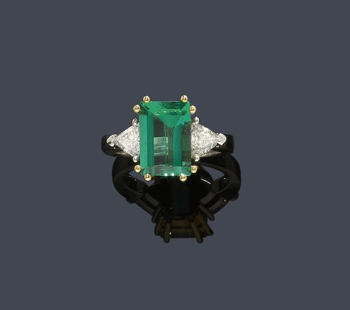 EMERALD AND DIAMOND RING. White and yellow gold 750. Classic-elegant ring, the top set with 1 very fine, step-cut Zambian emerald of 3.47 ct, in a yellow gold chaton, flanked by 2 triangle-cut diamonds weighing ca. 0.60 ct. Size ca. 54. With copy of SSEF Report No. 28575, October 1995 and Gübelin liquidation estimate, October 2005.