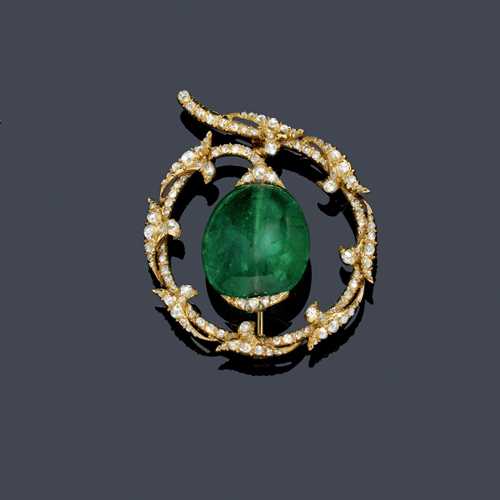 EMERALD AND DIAMOND BROOCH, ca. 1920. Yellow gold. Round, ring-shaped brooch, decorated with appliquéd leaf motifs set throughout with numerous rose-cut diamonds weighing ca. 1.00 ct, the centre set with 1 very fine, donut-shaped, drilled Columbian emerald of ca. 30.00 ct. Ca. 4 cm Ø.