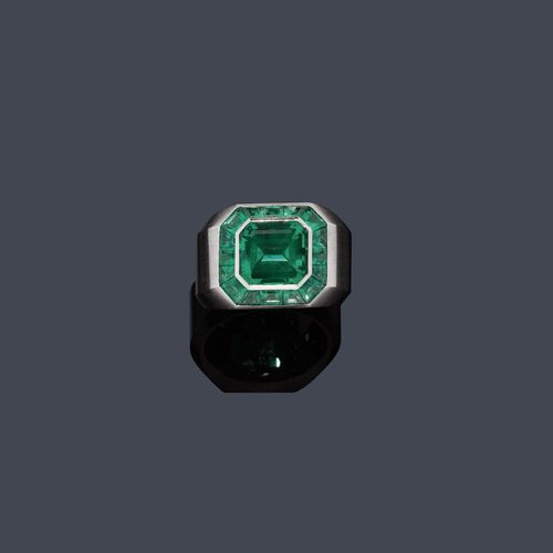 EMERALD AND GOLD RING, HEMMERLE. White gold 750. Casual-elegant, matte-finished band ring, the top set with 1 very fine, octagonal, Columbian emerald of 4.00 ct, within a border of 16 square-cut and trapeze-cut emeralds weighing ca. 2.00 ct. Size ca. 59. With copy of Gübelin certificate No. 73Z-12189-17, June 1971. Oral estimate by GGTL/Gemlab.