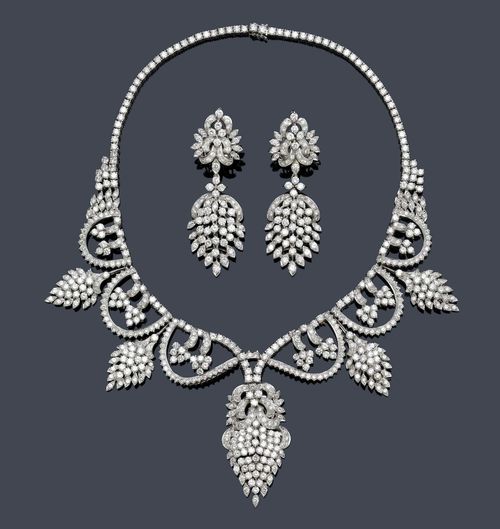 DIAMOND DEMI-PARURE, ca. 1960. White gold 750 and platinum 900. Elegant, decorative Rivière necklace, the front additionally decorated with garlands and stylised blossoms, set throughout with ca. 580 brilliant-cut diamonds weighing ca. 26.00 ct in total. L ca. 40.5 cm. Matching ear pendants with clips and studs, set throughout with numerous brilliant-cut diamonds weighing ca. 5.00 ct, L ca. 6.5 cm, and ring with blossom-shaped, diamond-set top weighing ca. 2.00 ct. Size ca. 52. Case signed Mirza M. Suleman & Sons. Karachi.