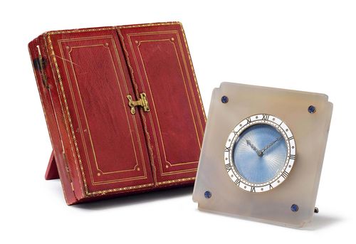 VERY FINE AND RARE CARTIER TABLE CLOCK, ca. 1915. Agate, gold and enamel. Square, polished agate disk, the four corners decorated with sapphire cabochons. Round, gold lunette with white enamel and gold Roman numerals. Engine-turned dial, enamelled light blue, with diamond-set arrow hands. Round, gold-plated watch case mounted on the back of the agate disk. Signed and numbered: Cartier, 96982. Gold-plated, silver folding base, numbered and signed: 96982 Paris 373. One knob for setting the time and one for winding the clock. 8-day movement with compensation balance and Breguet spring.  D 92 x 92 mm. This very fine &quot;Montre de Bureau&quot; comes with the original Cartier case in red leather embossed with gold. The leather case likewise has a foldable base, enabling the clock to be set-up and shown in the case as well. D 120 x 120 mm. With original case by Cartier.