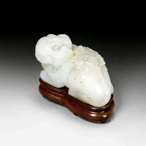 A PALE CELADON JADE CARVING OF A MYTHICAL BEAST WITH PEONIES. China, Qing dynasty, width 8.8 cm. White inclusions. Wood stand.