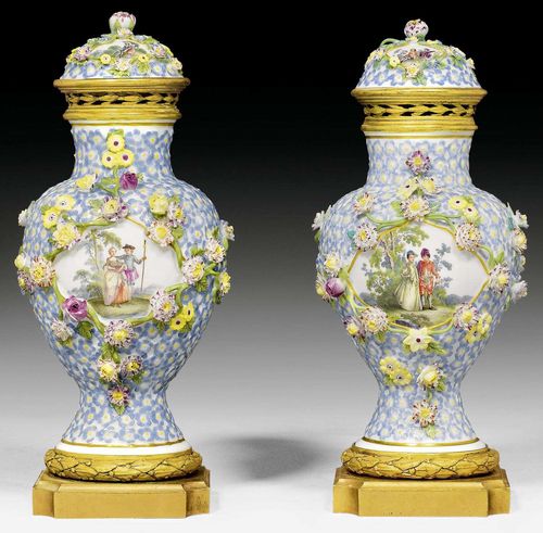 PAIR OF COVERED VASES WITH GILT BRONZE MOUNTS, MEISSEN, CIRCA 1750.Decorated with forget-me-nots in relief, landscape reserves with Watteau-style scenes on both sides and applied trailing flowers. The gilt bronze mounts with pierced lid. Underglaze blue sword mark on the underside of the plinth. H 24.5cm. Minor chips on the flowers and leaves. The lid fixed. (2)