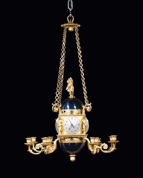 IMPORTANT CHANDELIER AND CLOCK WITH 4 DIALS,Empire, from a Paris master workshop, circa 1810. Matte and polished gilt bronze and blue-painted brass. The chandeier decorated with putti and suspended on 4 chains ceiling crown. The clock with enamel dial and fine movement "à complications" on three levels, with "échappement à balancier cicurlaire" and  4/4 striking on 2 bells. H 95 cm, W 75 cm. Provenance: - formerly collection of the Maréchal and Comte Jean Rapp (Colmar 1771-1821 Rheinsweiler). - from a European collection.