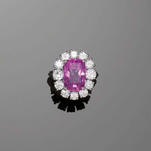 PINK SAPPHIRE AND BRILLIANT-CUT DIAMOND RING, E. MEISTER, ca. 1970. White gold 750. Fancy Entourage model, the top set with 1 fine, antique-oval pink sapphire of 8.26 ct, untreated, surrounded by 12 brilliant-cut diamonds totalling ca. 1.96 ct. Size 53. Matches the previous lot. With Gemlab Report, No.1612/08, April 2008.