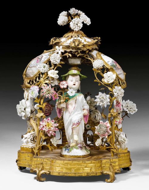IMPORTANT TABLE ORNAMENT "A LA PAGODA", Louis XV, the figure and plaques after J.J. KAENDLER (Johann Joachim Kaendler, 1706-1775), the flowers probably from the Vincennes factory, the bronze probably from a Paris master workshop, circa 1760. Porcelain boy with movable head. Porcelain plaques with idealized park landscapes and gallant scenes after J.A. Watteau. The figure minimally repaired, smaller chips. H 47 cm. Provenance: - Important private collection, Switzerland. - Sotheby's Zurich Auction on 10.12.1996 (Lot No. 358). - Private collection, Kusnacht (ZH). - Galerie Koller Auction on 8.9.1999 (Lot No. 1599). - From a highly important European private collection.