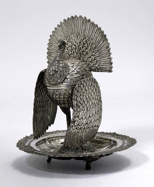 BONBONNIÈRE DESIGNED AS A TURKEY,silver. Unmarked. Probably 20th century. Hinged body with embossed plumage (pin missing). Movable wings on both sides. On a round, three-footed plate with open-worked rim all around. Eyes of red gemstones. H 31.5 cm, 1437 g.