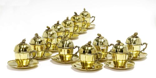 12 SILVER-GILT, COVERED CUPS WITH SAUCERS,20th century. Conical, with vertical embossing. Matching, convex lid, finial with petals. Curved handle. H 17.5 cm. Total weight: 6240 g.