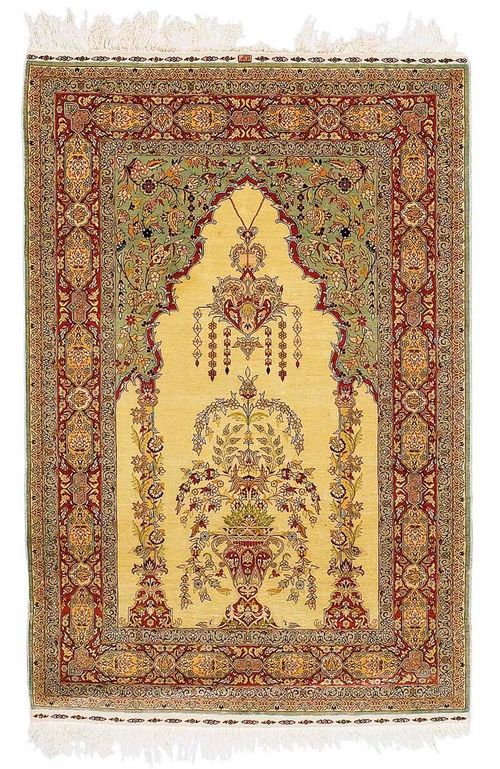 HEREKE SILK prayer rug, signed.Very fine item with a beige mihrab and light green spandrels, the mihrab is flanked by two columns; the entire carpet is finely decorated with floral wreaths in attractive pastel colours, red border with floral cartouches, slightly stained, otherwise in good condition, 135x90 cm.