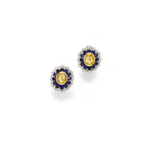 SAPPHIRE AND DIAMOND EAR CLIPS. White gold 585. Classic-elegant ear clips, each set with 1 antique-oval, yellow sapphire within a double-border of 12 round, blue sapphires and 24 brilliant-cut diamonds. Total weight of the sapphires ca. 8.90 ct and total weight of the diamonds ca. 1.50 ct.