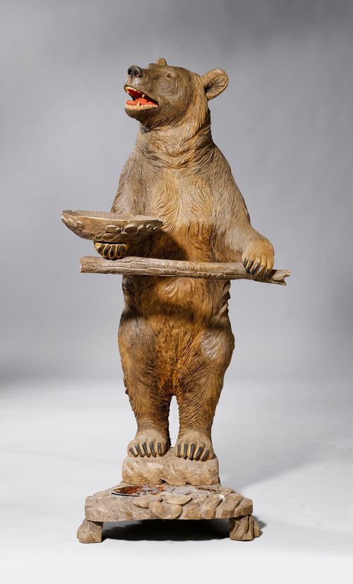UMBRELLA STAND DESIGNED AS A BEAR,Brienz, ca. 1900. Hardwood (probably lime tree), carved all-around and stained. On an oval base with an umbrella stand and vide-poche. H 121 cm. Some cracks.