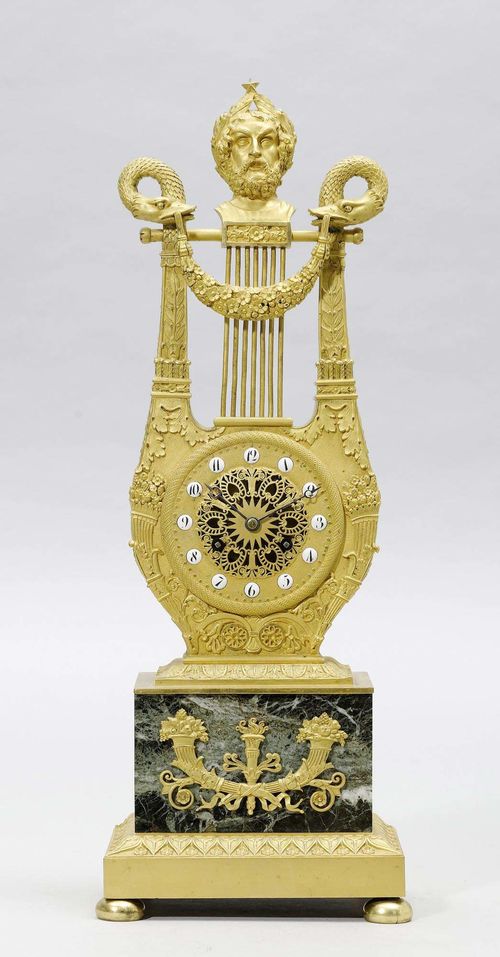 LYRE CLOCK, Restoration, Paris ca. 1830. Bronze. Case designed as a lyre, the top crowned with the head of Apollo, framed by 2 snake heads. Open-worked dial with white enamel cartouches. Hook movement striking the ½-hour on bell. H 50 cm.