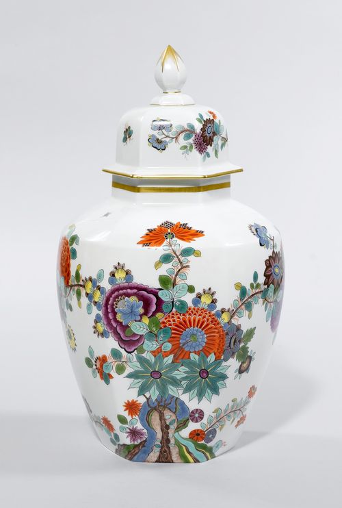 LIDDED VASE WITH ORIENTAL FLORAL DECORATION,Meissen, after 1934, second quality. Polygonal vase, opulently painted with Indian flowers growing on a cliff, and flying insects. Underglaze blue sword mark with 2 incisions. H 43 cm. (2)