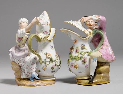 PAIR OF JUGS DESIGNED AS A FARMER AND A PEASANT WOMAN,Meissen, ca. 1900. Young man wearing a black hat, and a purple patterned jacket over leather-colour knickerbockers, sitting a on a rock. The girl wearing a peasant dress patterned with pink flowers, and a head scarf. Both figures holding the lid of their jug open. Underglaze blue sword marks with pommels, model number 907 and 1234. incised. H 19 cm. One thumb repaired.