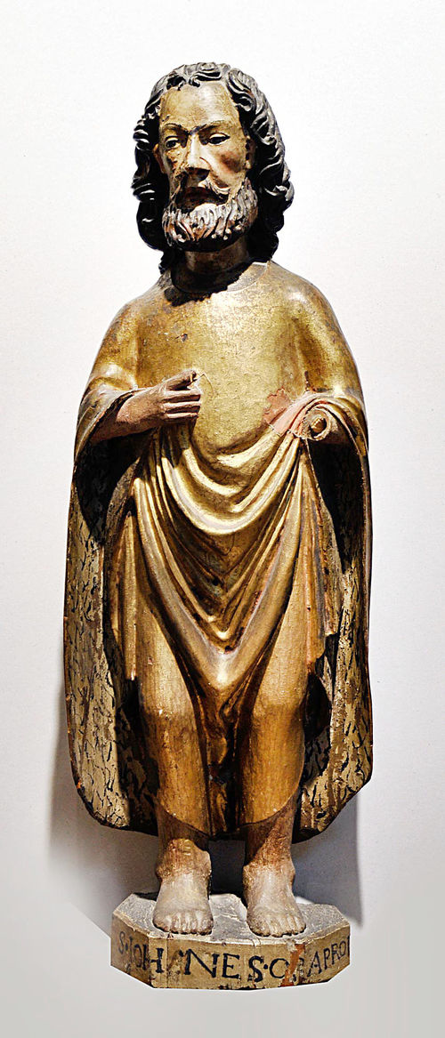 JOHN THE BAPTIST,Southern Europe, early 15th century. Pinewood, carved and painted. The saint is standing on an inscribed base and wearing a cloak. H 85 cm. Left hand missing.