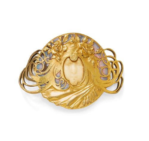 ENAMEL CLIP BROOCH, PIEL FRERES, ca. 1900. Very attractive, gold-plated Art Nouveau brooch designed as a belt buckle, decorated with 1 sculptured head of a woman with flowers in her flowing hair, the face of carved bone, the background finely enamelled in shades of lilac. Enamel with signs of wear. Mechanical part in gold, not original. Ca. 7.8 x 5.5 cm. A very similar belt buckle is depicted in the catalogue: Art Nouveau Buckles, Jugendstil-Gürtelschliessen 1896-1910, Sammlung Kreuzer, Hg. Jo-Anne Birnie Danzker, Stuttgart, Arnold 2000, ISBN 3-89790-151-X