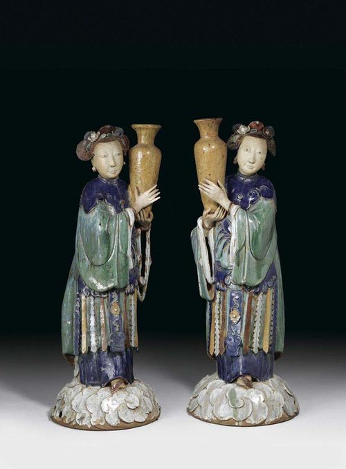 PAIR OF DECORATIVE CERAMIC LADIES, each one holding up a flower vase. They are standing on clouds and wearing dark-blue ruyi collars over green robes. Their bound feet peak out from under the hem of their undergarments. Delicate oval faces, pinned hair decorated with flowers. China, 18th/19th century, H 85 cm. Slightly restored. (2)