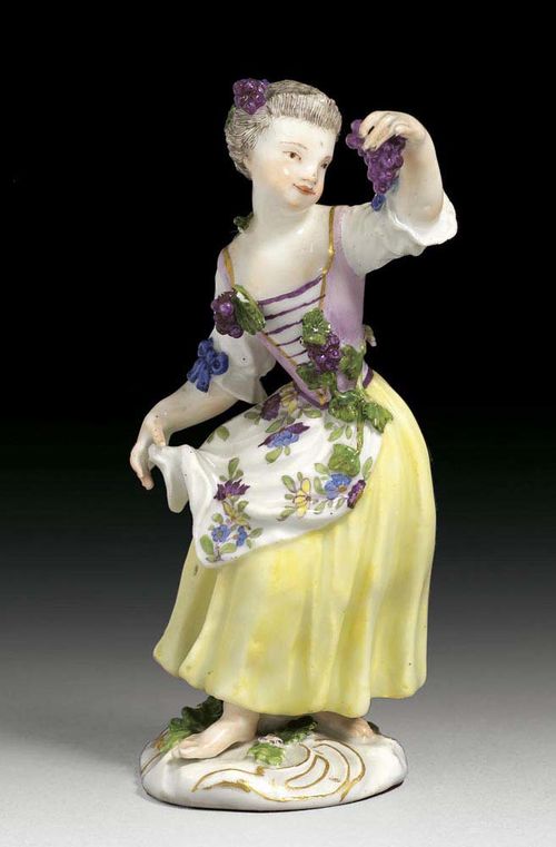 GIRL WITH GRAPES, Meissen, um 1750. With a violet waist coat applied with grapes, over yellow skirt with flowered apron and wine in her left lifted hand, crossed swords in underglaze-blue, 13cm, slightly chipped.