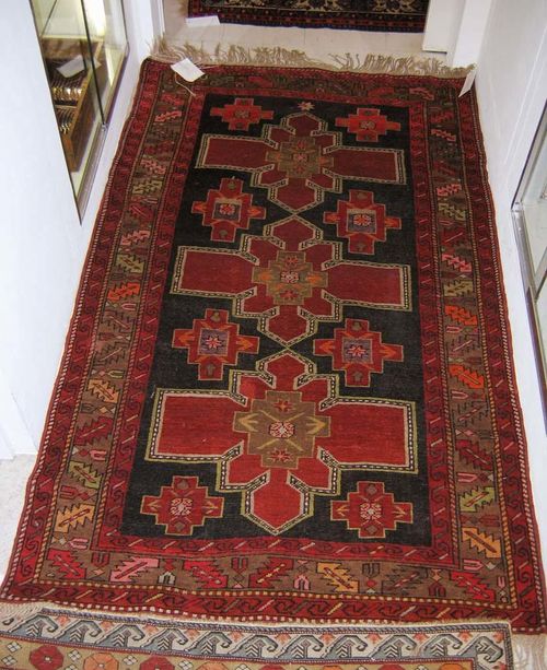 KAZAK, old. Black ground with 3 rust red flower-shaped medallions and triple stepped wineglass border. Good condition. 196x116 cm.