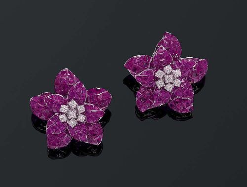 RUBY AND BRILLIANT-CUT DIAMOND CLIP EARRINGS. White gold ca. 670. Highly decorative clip/stud earrings in the shape of a flower, set with numerous carré-cut rubies totalling ca. 21.65 ct, invisible-setting, and additionally decorated with 14 brilliant-cut diamonds at the centre totalling ca. 0.70 ct.