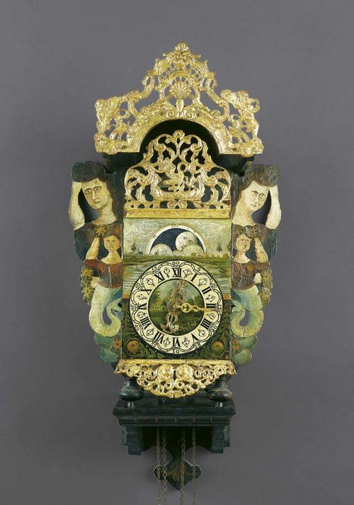 PAINTED IRON CLOCK WITH MOON PHASES AND PLINTH,Baroque, Friesland, 18th century. Portal-shaped wall plaque, with pierced cornice, decorated with sirens and shaped plinth. Rectangular clock case with pierced front, painted chapter ring, fine verge escapement with iron wheels, striking the 1/2 hours on 2 bells. Wall plaque 83x40x28 cm, clock 33x15x48 cm. Provenance: Private collection, Switzerland