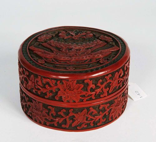 ROUND CONTAINER WITH LID made of carved lacquer in red, black and brown layers. On the lid: finely-decorated bowl filled with precious items with a large lotus bud in the middle. The peach of immortality lies in the middle of this bud with the two boys He and He on either side. (The boys' names are pronounced slightly differently in Chinese.) The boys symbolize harmony. On the side: lotus tendrils on a geometric background. China, 18th/19th century. D 11.5 cm.