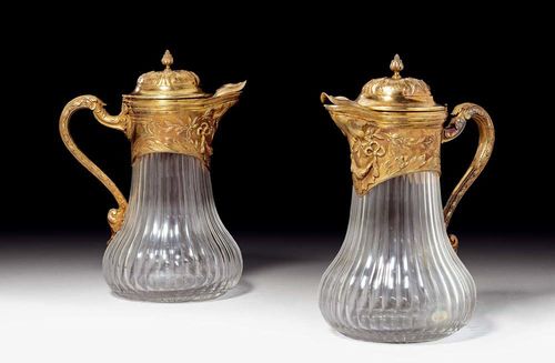 PAIR OF CARAFES WITH SILVER-GILT MOUNT. Paris, 19th century. Glass. The neck with a silver-gilt mount with laurel and acanthus leaves and festoons. The covers with acanthus leaf rosette and floral finial. Curved handle. Beak spout with engraved crown. H 25 cm.