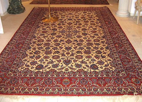 ISFAHAN. Beige ground, patterned with trailing flowers and palmettes in red and blue tones, red border, good condition, 329x210 cm.